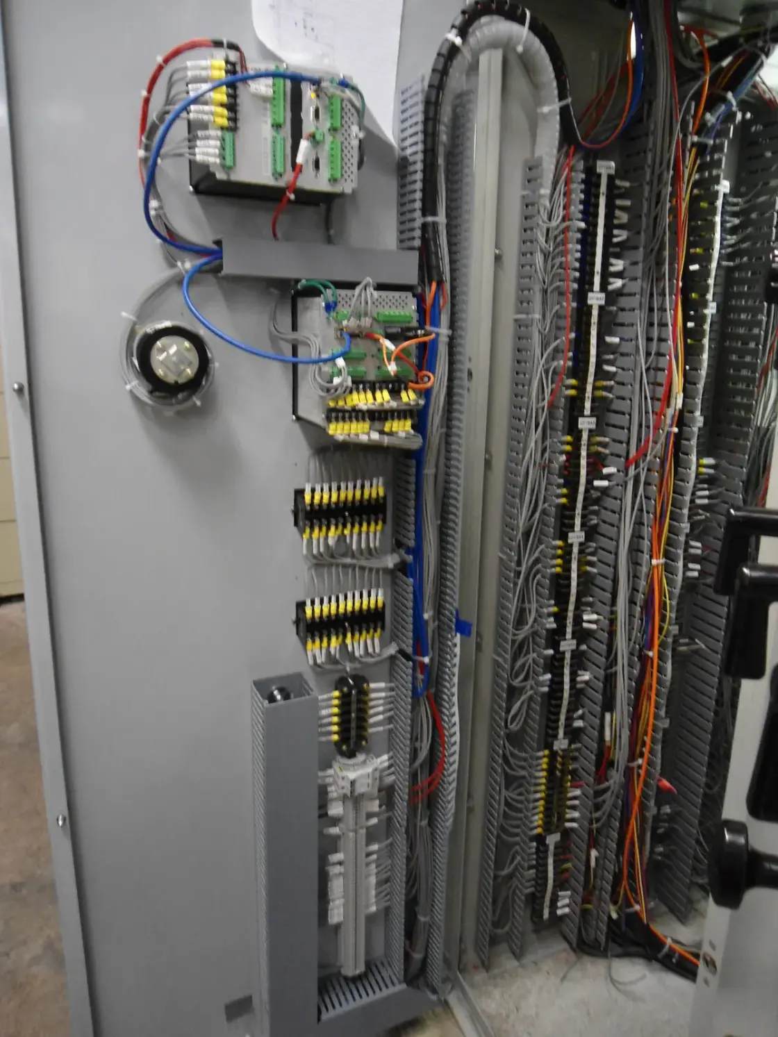The open interior of a control panel showing rows of numbered terminal blocks and bundled field wiring