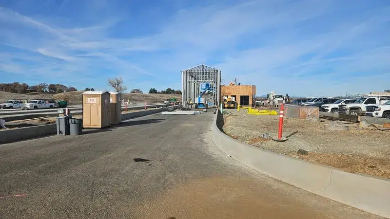 A weigh station building and canopy beside a paved truck lane, with construction materials on site