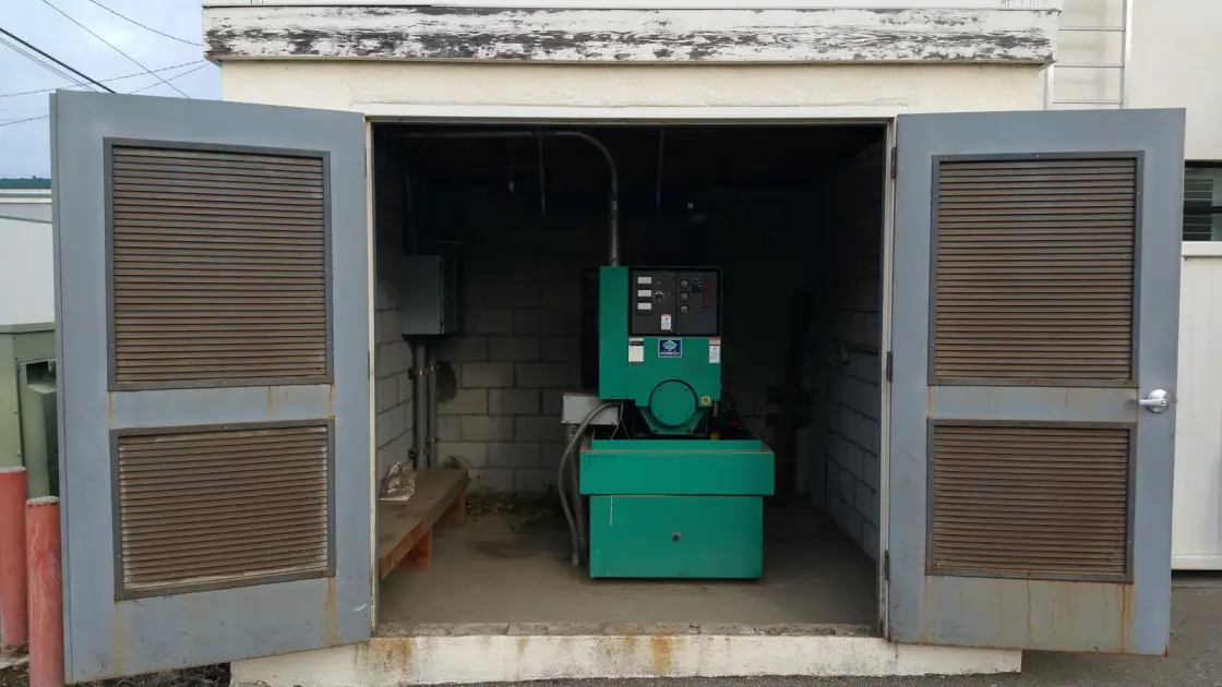 A standby generator installed inside a masonry enclosure with louvred doors open to the front