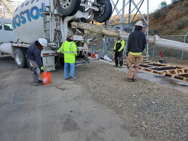 A concrete truck discharging down a chute while a crew places and screeds concrete at a substation
