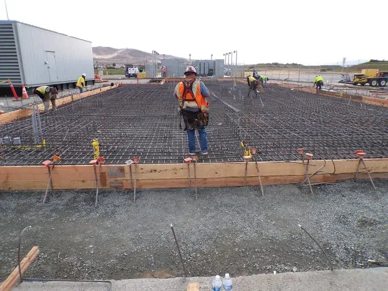 A worker standing on a large tied reinforcing steel mat inside timber formwork