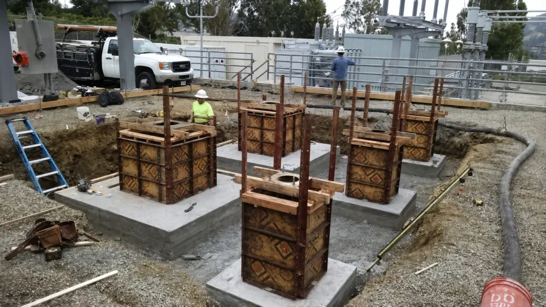 Square timber column forms with reinforcing steel projecting, set on new concrete pads at a substation site