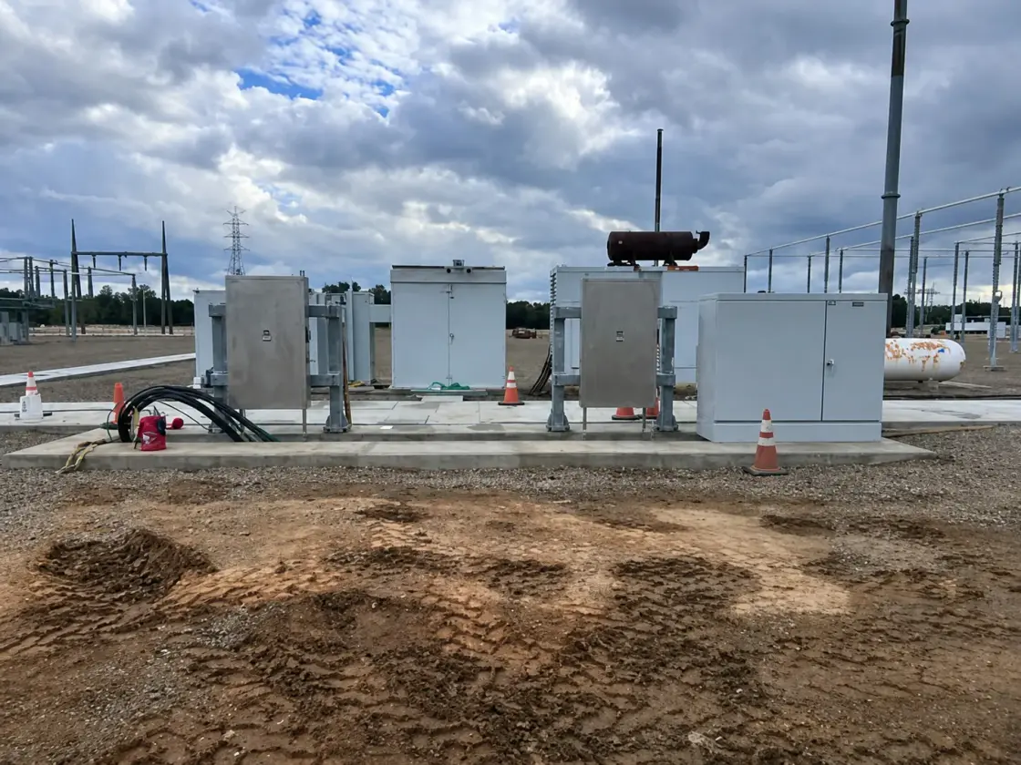 Several grey metal-clad electrical cabinets standing on a new concrete pad in a substation yard under a cloudy sky