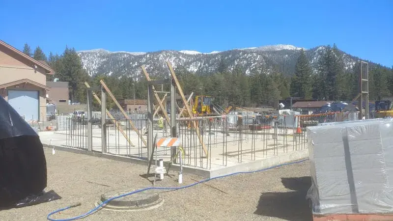 Timber formwork and reinforcing set on a concrete pad at a treatment plant, with snow-capped mountains behind