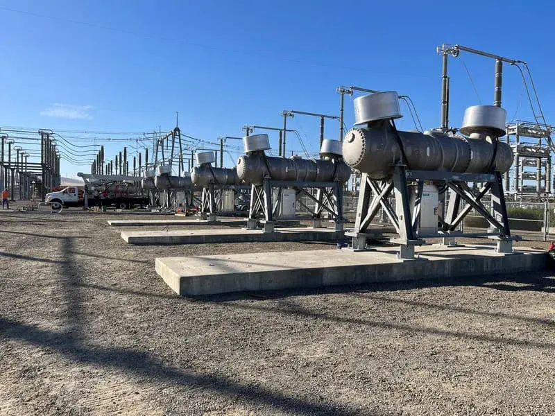 Three large capacitor units mounted side by side on steel stands in a substation yard