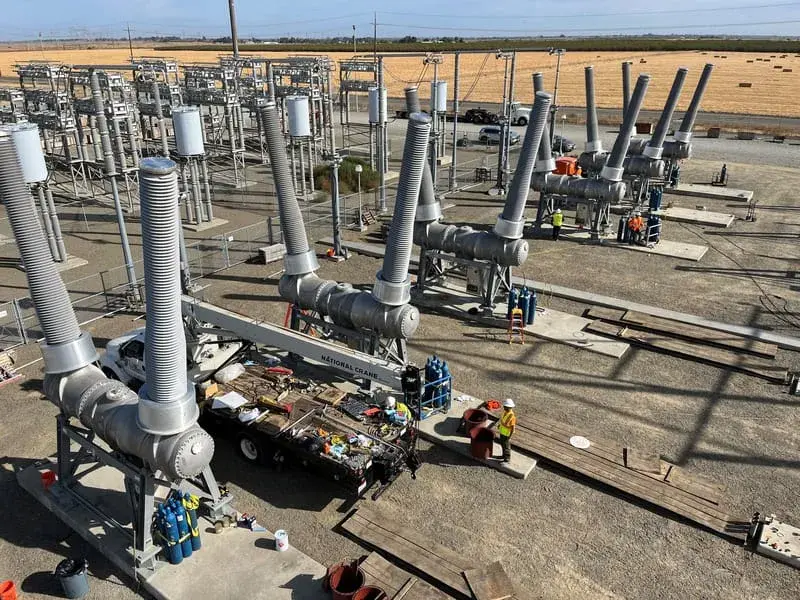An elevated view along a row of substation equipment with crews and materials laid out along the bay