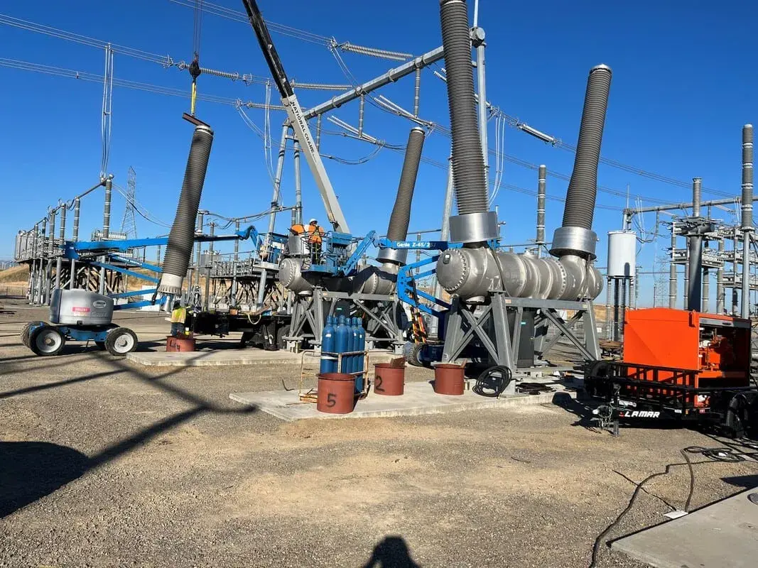 Substation bay under construction with a crane, a boom lift and crews working beneath large 500kV bus insulators