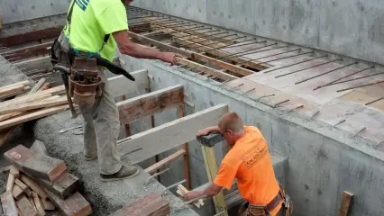Two workers laying timber forms across the top of a poured concrete structure
