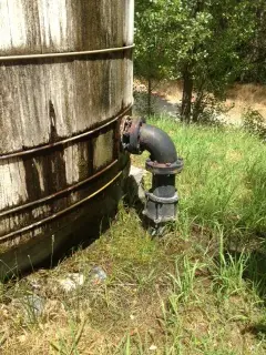 A flanged pipe elbow and valve emerging from the ground beside a narrow track