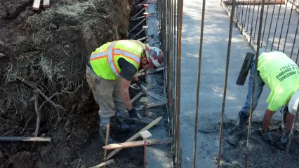 Two workers in high-visibility clothing working along a concrete wall line between reinforcing bars