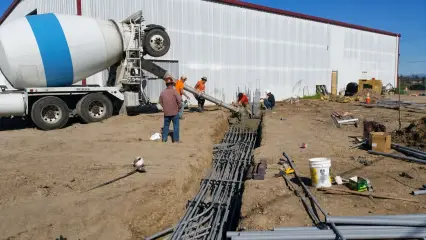 A concrete truck discharging down its chute to a crew working in a trench beside a building