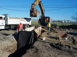An excavator loading a dump truck beside an open excavation at a wastewater treatment plant
