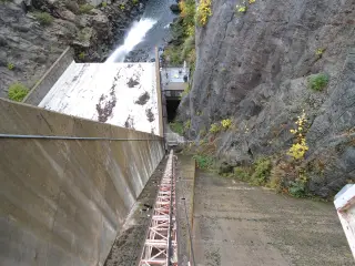 The curved concrete face of a dam in a rock canyon with a steep incline railway running down beside it