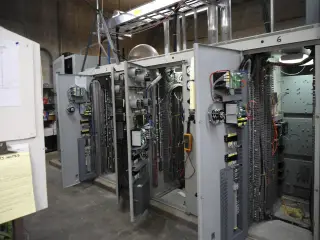 A row of grey control cabinets standing open inside a powerhouse, their interiors exposed