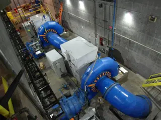 A view from above of a hydroelectric powerhouse floor with large blue penstock pipes running to turbine casings