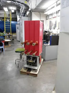 A red switchgear unit on a wooden pallet with copper bushings across its face