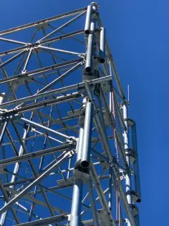 A galvanised lattice tower seen from below against a deep blue sky