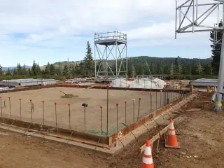 A large formed foundation with anchor bolts set, and a steel lookout tower standing behind