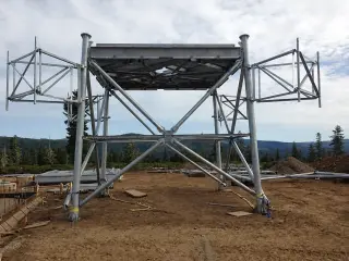 A heavy steel platform on splayed legs standing on a mountaintop, with forested ridges beyond