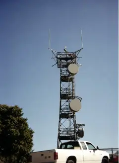 A steel lattice communications tower with two microwave dishes and antenna arrays against a clear sky