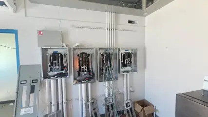 A room with several electrical panels and enclosures mounted on a white wall, conduit dropping from above