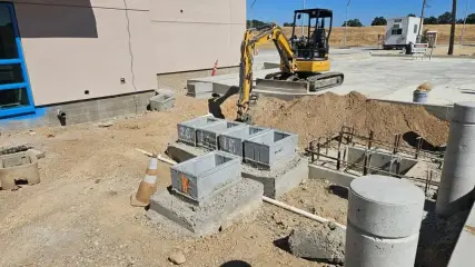 Concrete pull boxes and a manhole ring set in an excavation with an excavator working behind