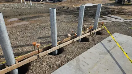 Three galvanised steel posts projecting from new concrete foundations beside a paved lane