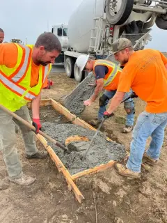 Two workers placing and working concrete from a truck chute into a formed light base