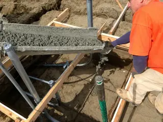 Concrete discharging down a chute into steel-supported formwork in a sandy excavation