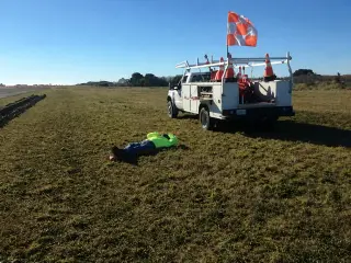 A utility truck carrying marker flags parked on the grass safety area beside a runway