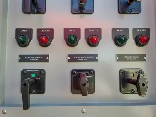 Rows of red and green indicator lights above black control switch handles on a switchgear panel