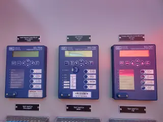 Three blue protective relays mounted in a row on a grey switchgear door, each with an engraved label above