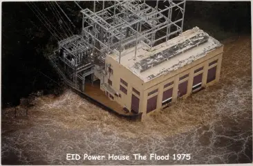 Aerial view of a powerhouse surrounded by brown floodwater, captioned EID Power House The Flood 1975