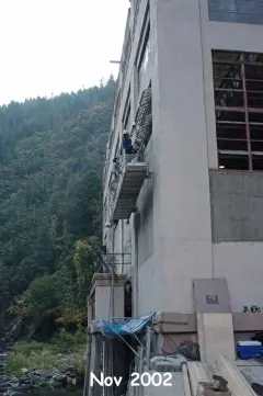 Scaffolding and staging against the concrete wall of a powerhouse in a steep river canyon