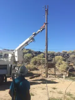 A line truck with its boom raised to a wooden distribution pole in open sagebrush country