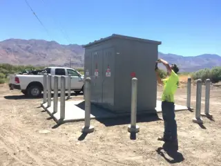 A worker at a grey padmount electrical enclosure on a concrete pad, with mountains in the distance