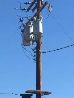 A wooden pole carrying a transformer and riser conduit, seen from below against a blue sky