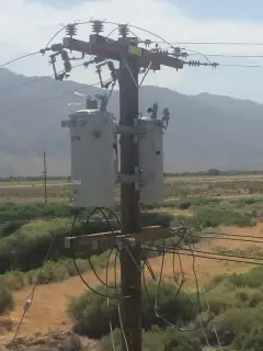 A wooden pole carrying a bank of distribution transformers and cutouts against a cloudy sky