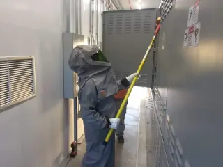 A worker in a full arc flash suit using an insulated tool at a wall-mounted electrical enclosure