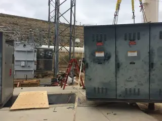 A crane lifting a metal-clad switchgear cubicle on yellow slings above a substation