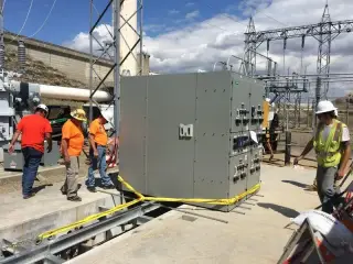 Several workers guiding a large grey switchgear cabinet along rollers onto its foundation