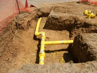 Yellow gas pipe runs and a tee fitting laid in a red-earth trench