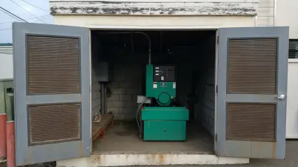 A standby generator installed inside a masonry enclosure with louvred doors open to the front