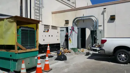 A generator set and a packaged unit standing on a paved area beside a building, cones set around them