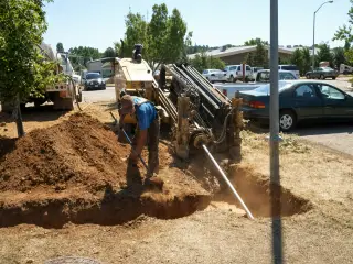 A worker digging by hand beside a horizontal directional drilling rig in a parking lot