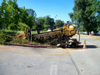 A yellow horizontal directional drilling rig positioned at the edge of a roadway