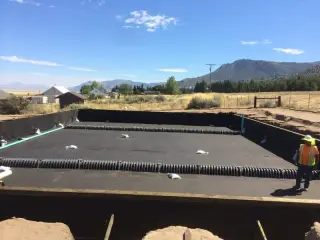 A wide lined basin with ballast sandbags spaced across the membrane under a clear sky