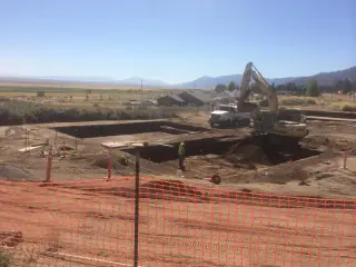 An excavator working in a large open excavation behind orange safety fencing