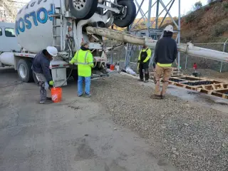 A concrete truck discharging down a chute while a crew places and screeds concrete at a substation