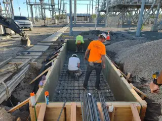 Two workers placing reinforcing steel inside timber formwork for a new equipment foundation